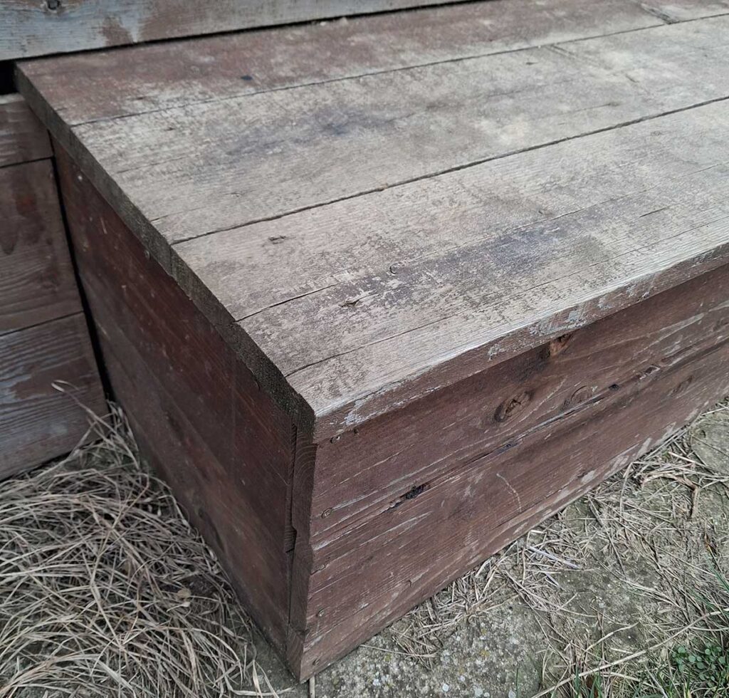 Close-up of a single metal stair step on a sloped deck: Rectangular tubing frame clad with matching wood decking boards for safe access down the elevation drop.